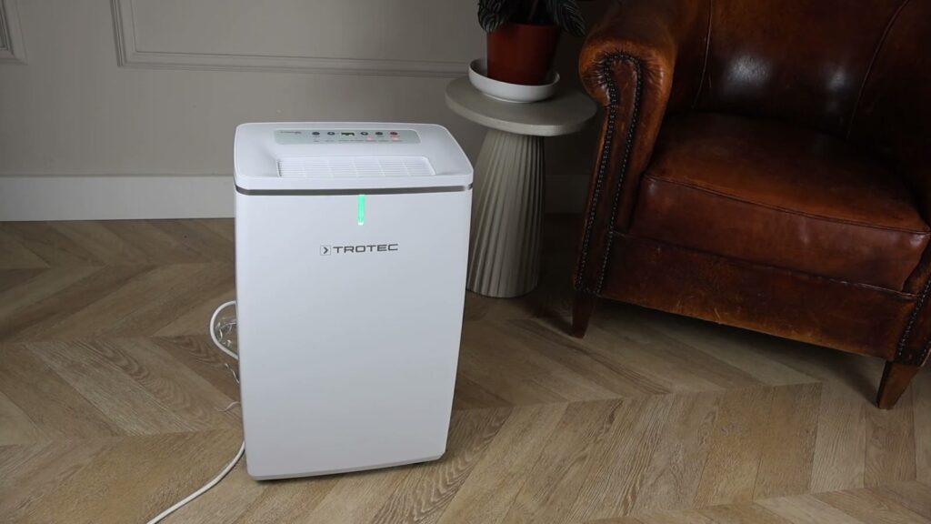 Luftentfeuchter Trotec TTK 72 E mit grün leuchtender LED neben einem Ledersofa